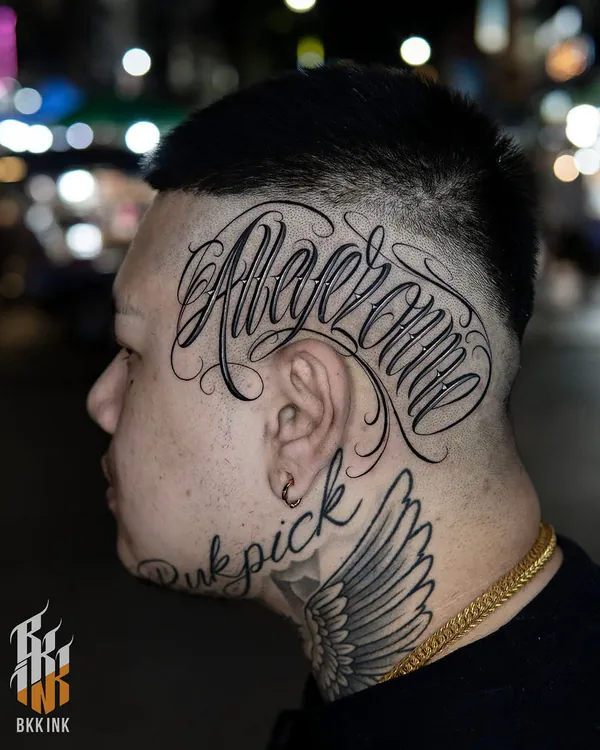 Elegant cursive script side head lettering tattoo Bangkok