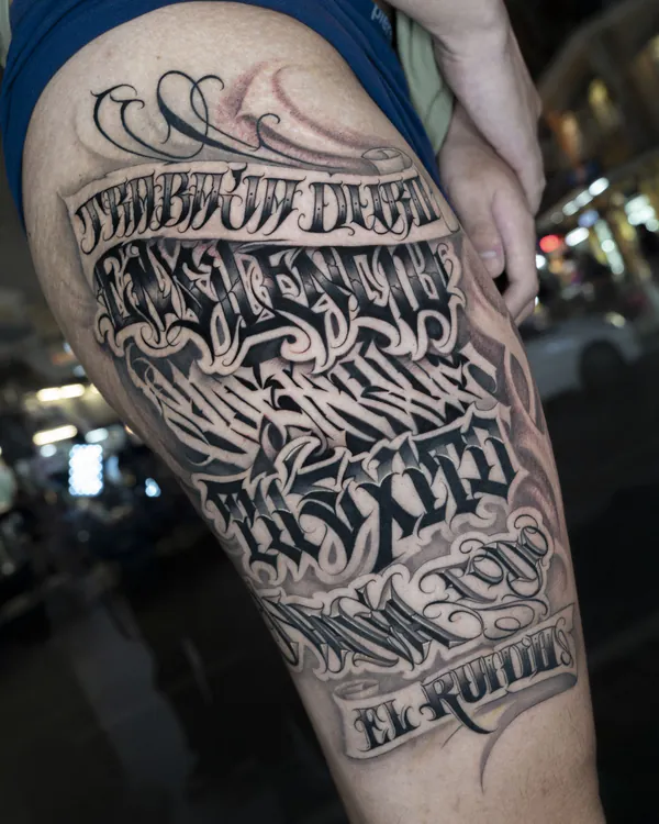 Multi-line gothic banner thigh lettering tattoo Bangkok