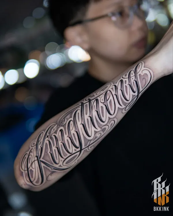 Delicate cursive script forearm lettering tattoo Bangkok