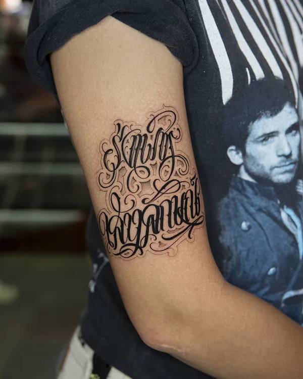 Flourished cursive script upper arm lettering tattoo Bangkok