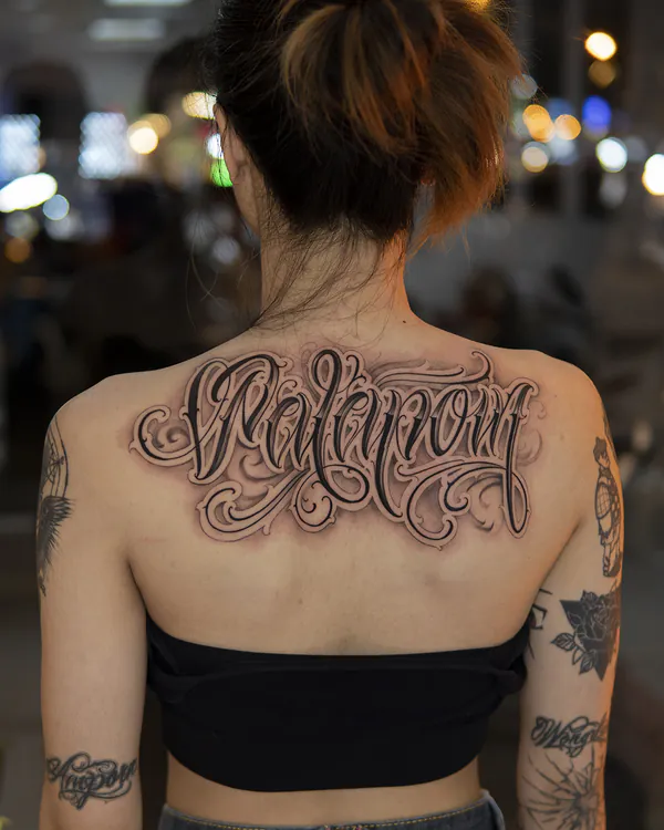 Elegant cursive script upper back lettering tattoo Bangkok