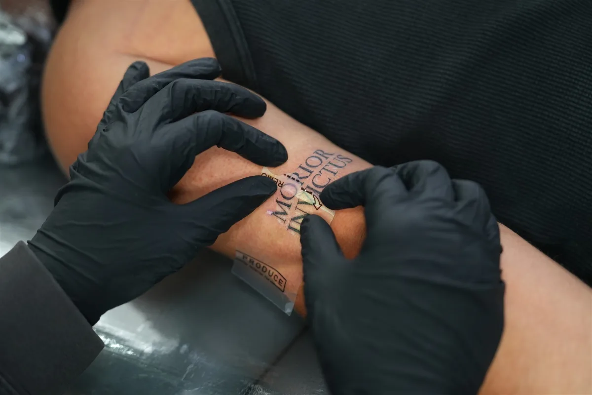 Tattoo artist smoothing a transparent second-skin protective film onto a new forearm tattoo at our Khaosan Road studio