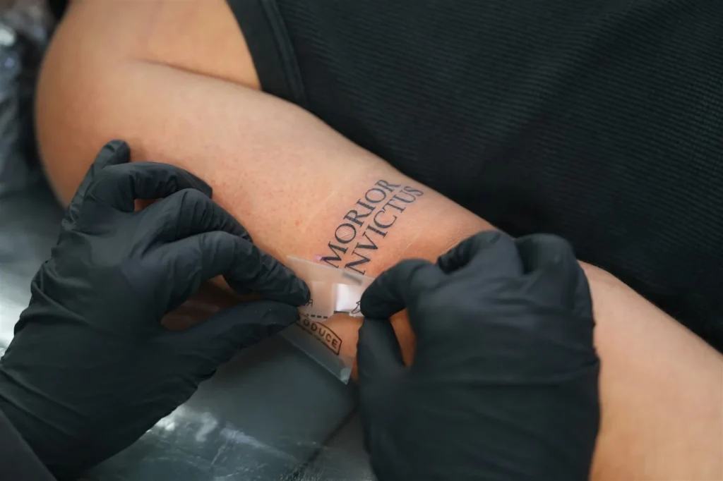 Gloved tattoo artist applying a second-skin adhesive film over a fresh lettering tattoo at BKK INK in Bangkok